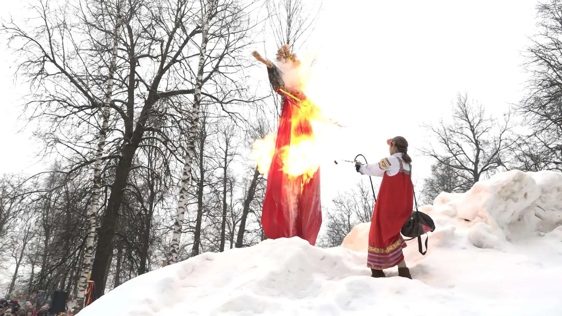 Девушка в русском народном костюме поджигает чучело Масленицы из огнемета в Сергиевом Посаде